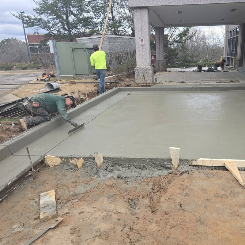 Workers troweling a large commercial slab beneath a covered entry