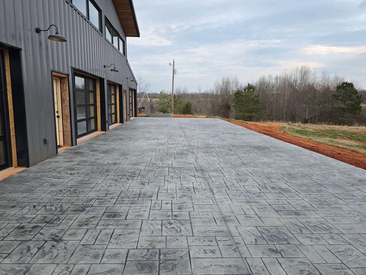 Ashlar-pattern stamped driveway leading to a metal-sided shop