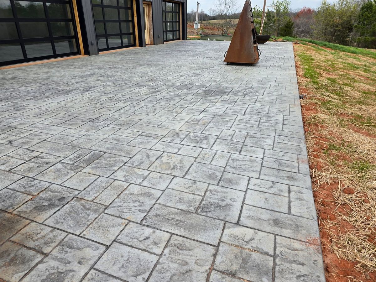 Steel sculpture standing on a stamped ashlar patio beside a glass-walled house