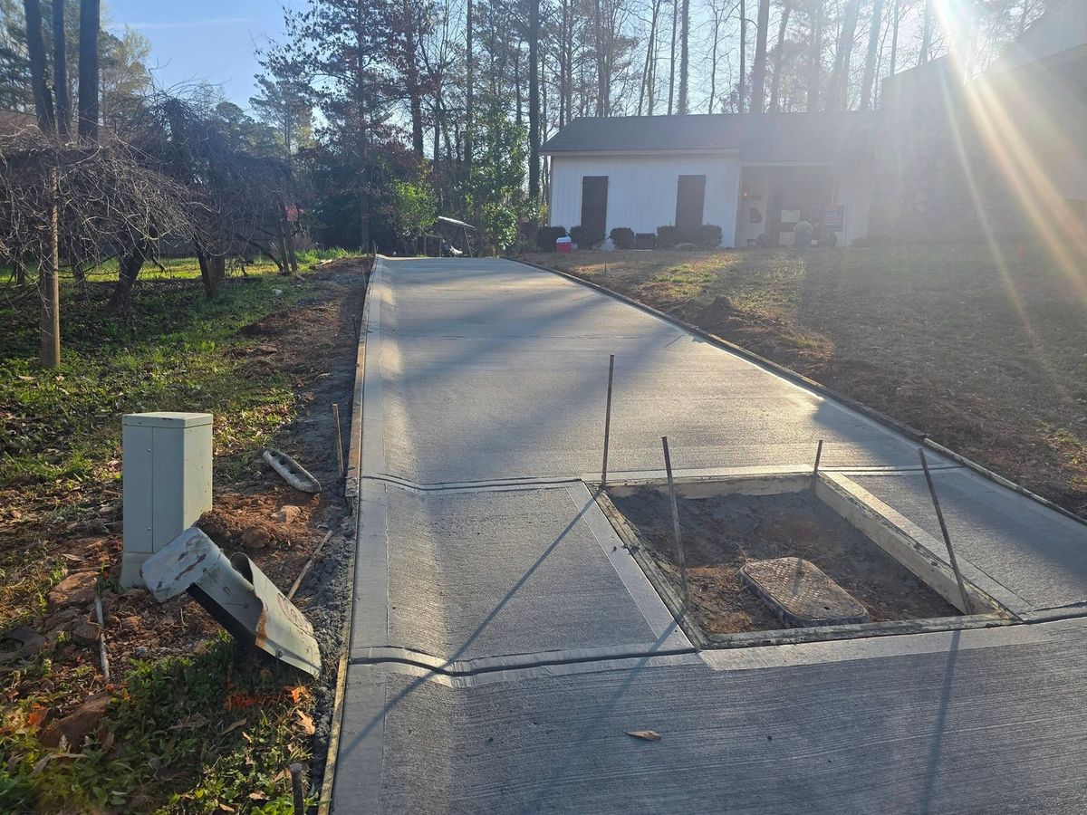 Wooded-lot concrete driveway with a boxed-out utility cover