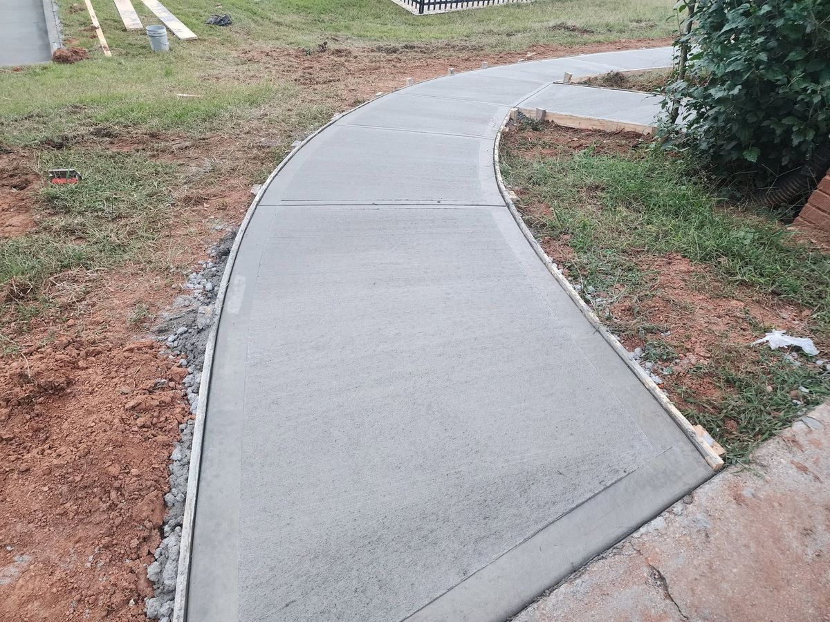 Newly poured curved sidewalk following a landscaped bank
