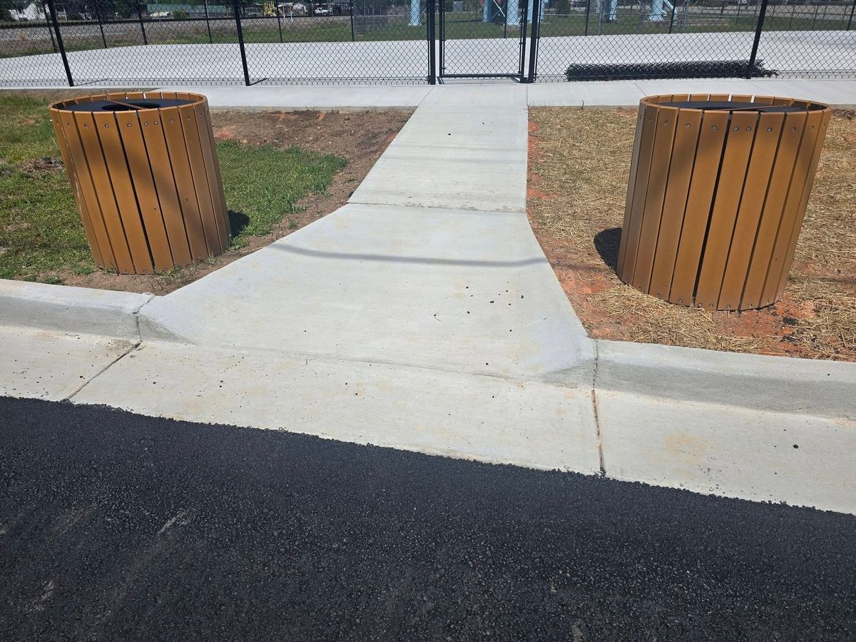 Park entrance walkway in new concrete between two trash bins