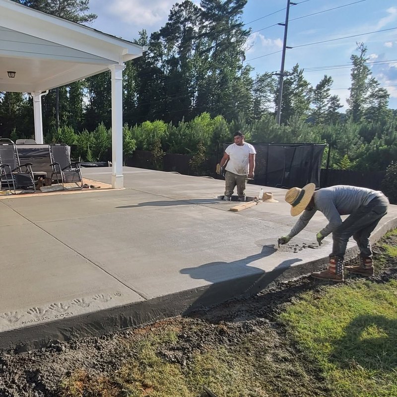 Two crew members finishing a new concrete patio under a covered porch