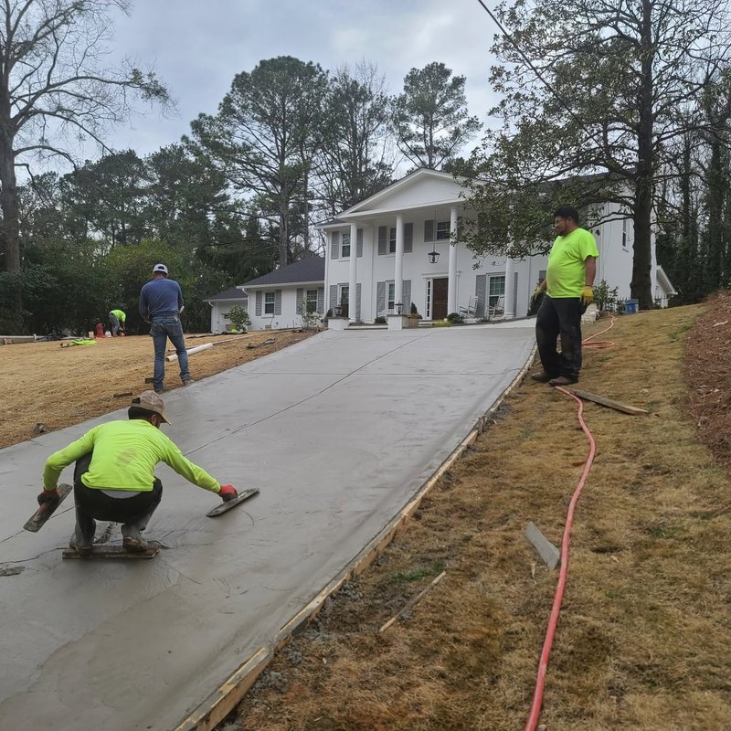Worker in a safety shirt kneeling to trowel a fresh driveway pour
