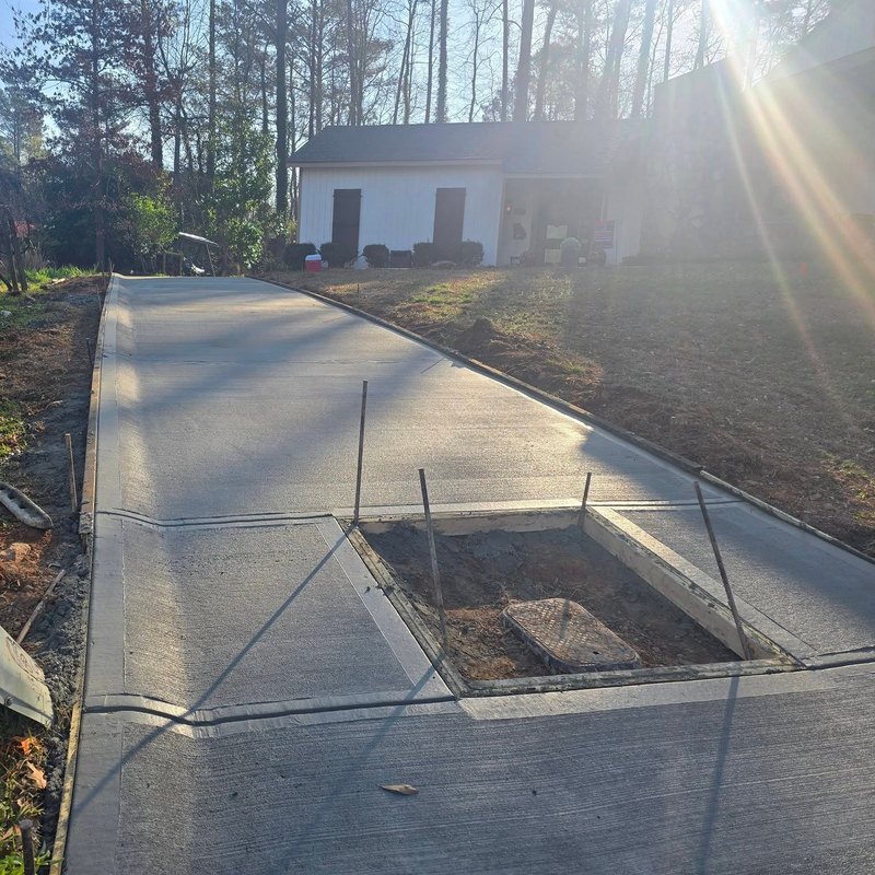 Fresh concrete driveway on a wooded lot, poured around a utility box