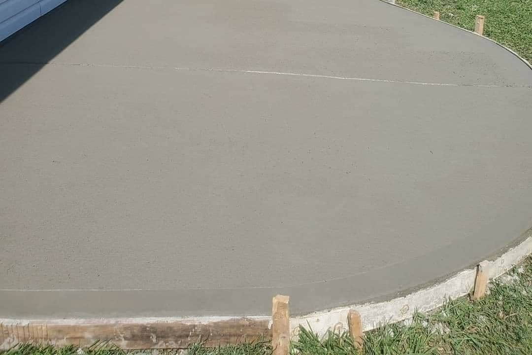 Broom-finished concrete patio poured behind a house with open fields beyond