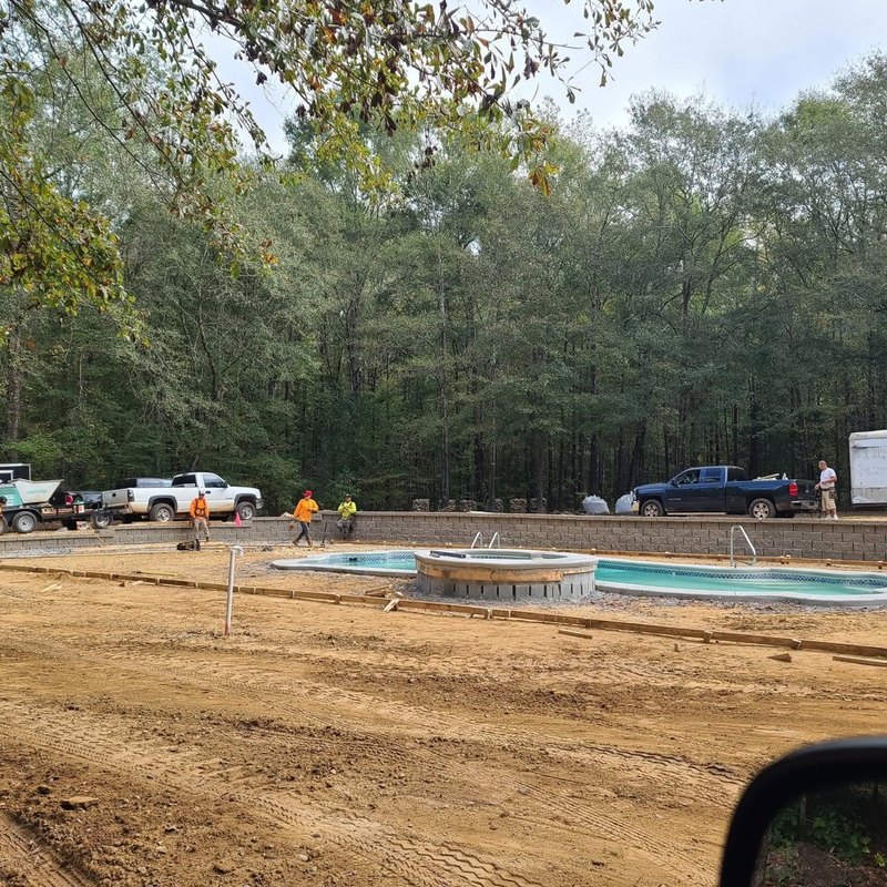 Forms laid out around a pool for a new concrete deck, work trucks in the background