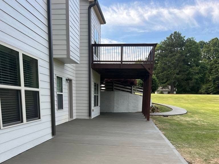 Broom-finished concrete patio wrapping under a raised deck behind a house