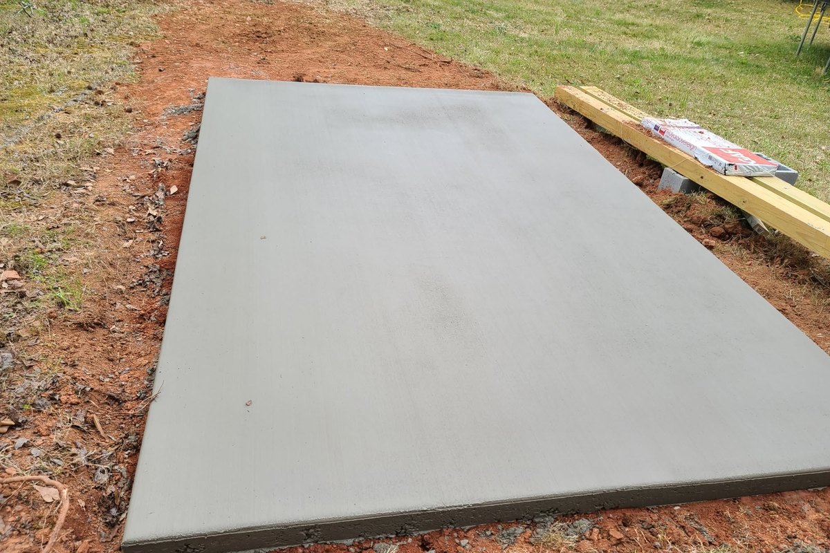 Cured concrete pad on red clay with form lumber stacked beside it