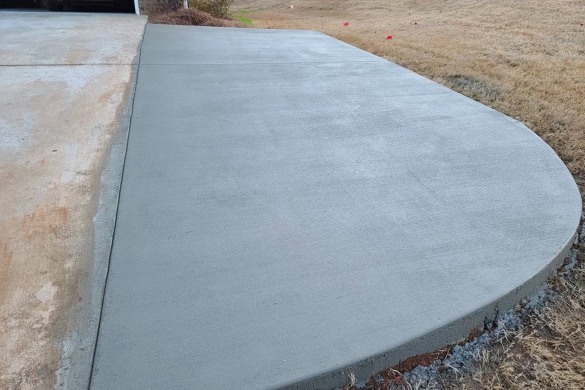 Broom-finished concrete pad added beside a driveway on a dry lawn