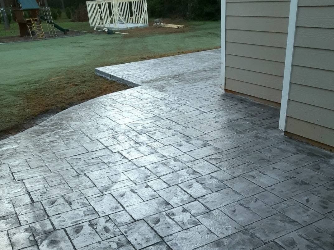 Slate-pattern stamped patio at the back of a house with a playset in the yard