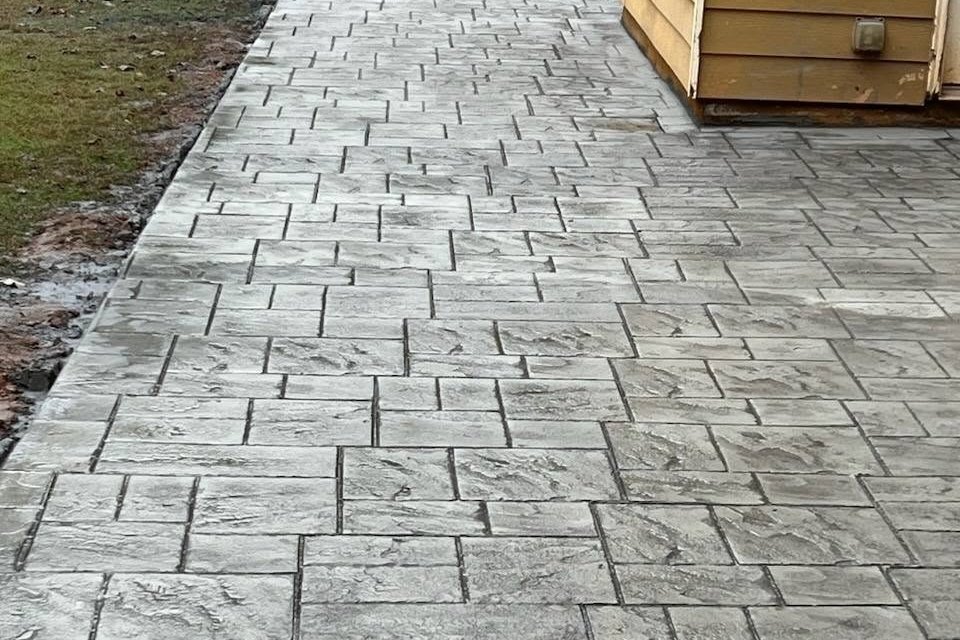 Ashlar-pattern stamped walkway running past the corner of an outbuilding